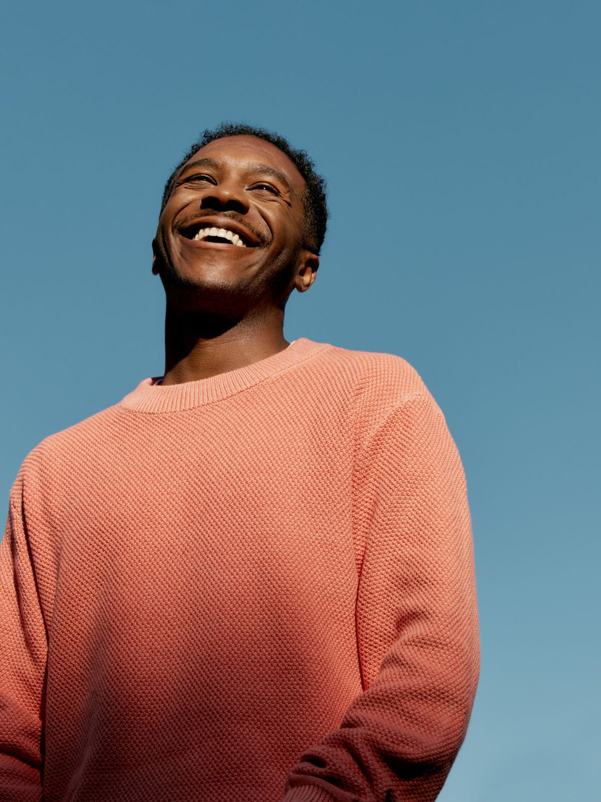 Smiling man in a coral sweater against a blue sky